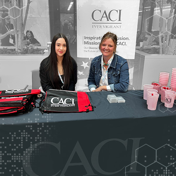 two women sitting behind a CACI table with CACI branded handouts