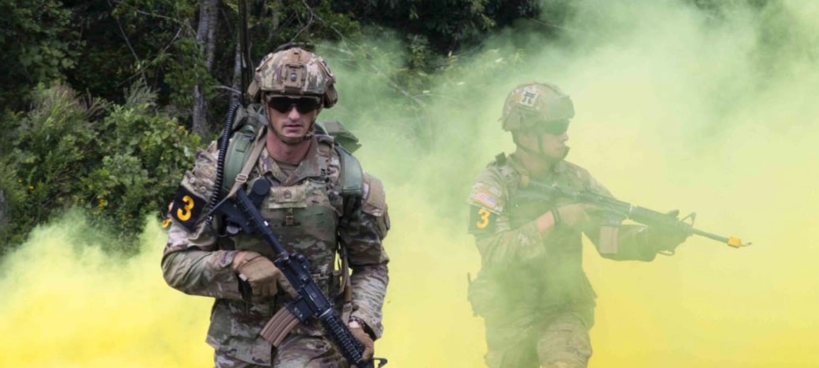 Two soldiers walking through colored smoke.