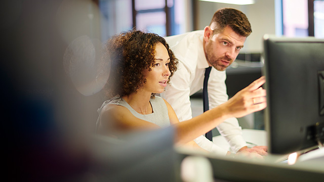 Two people in a professional office setting focus on a computer screen.