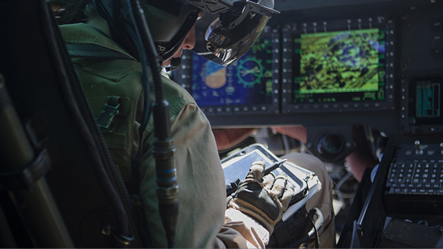 Pilot in a cockpit with helmet and gloves, focusing on a digital tablet.