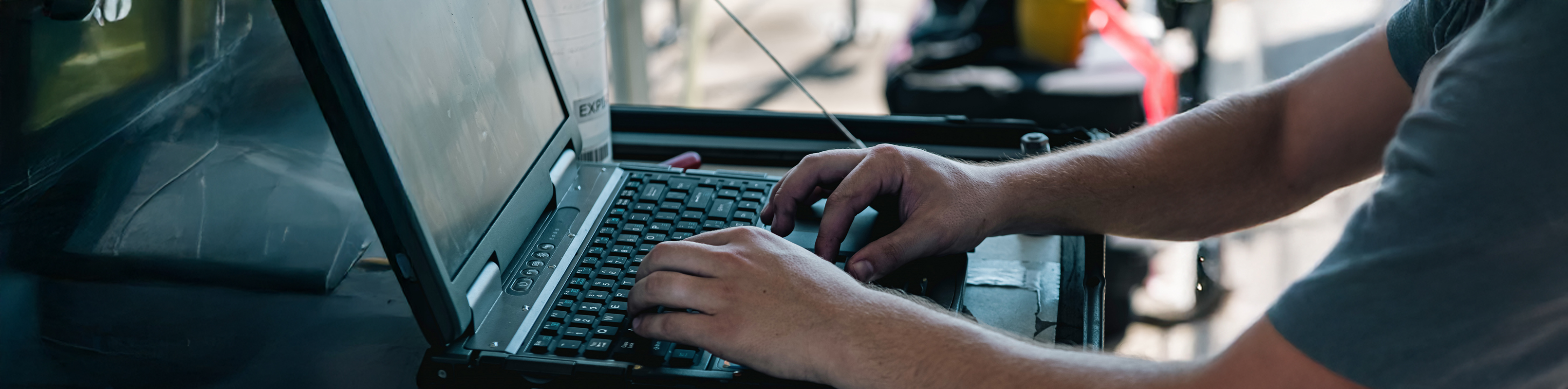 A man focused on typing on a laptop computer, with a neutral background and a desk in view.
