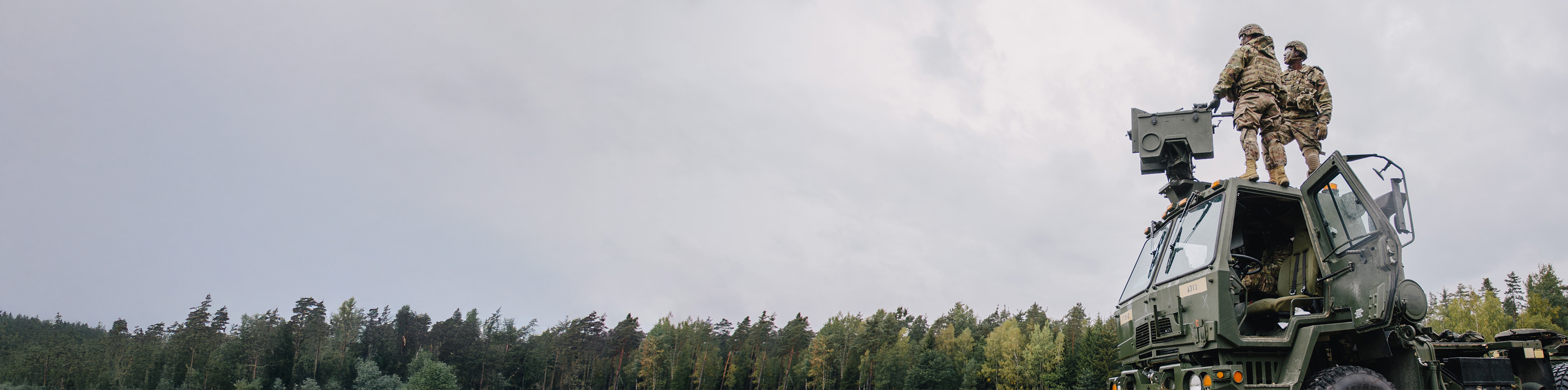 A military vehicle with a man standing confidently on top, surveying the surroundings.