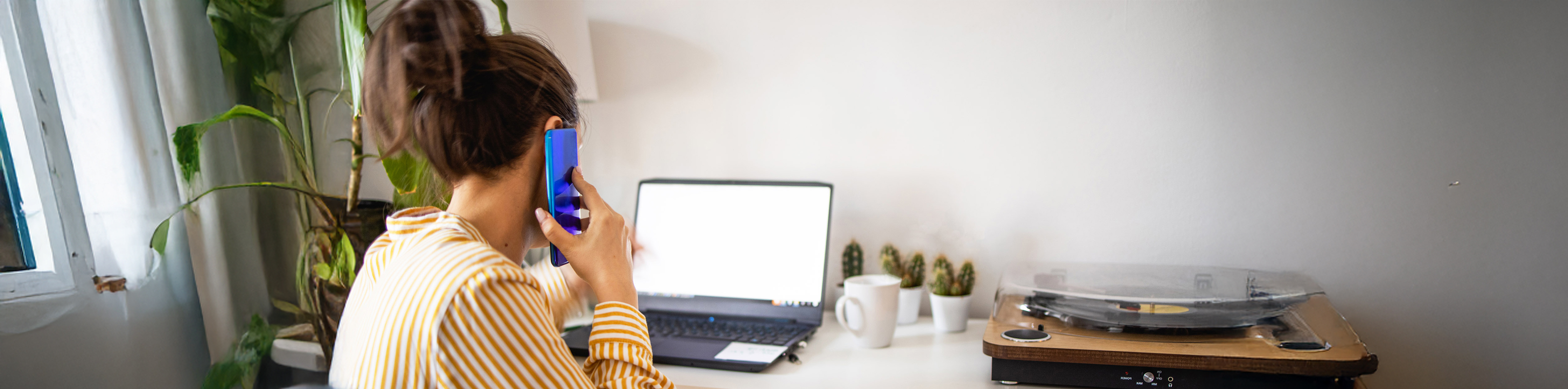 A woman sits at a desk, focused on her laptop, with a notepad and pen beside her.