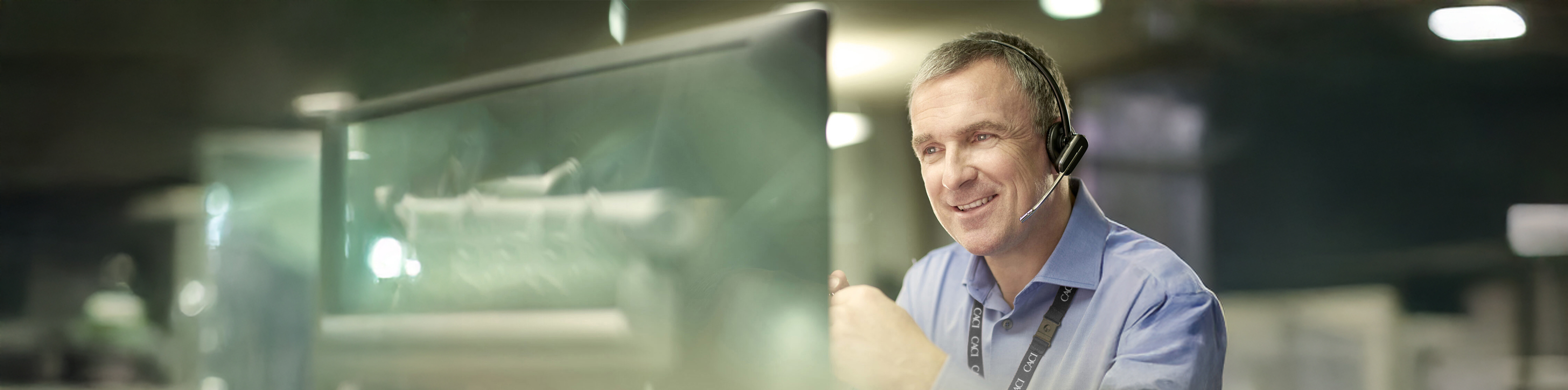 A smiling man stands in front of a large monitor, showcasing a positive and engaging atmosphere.