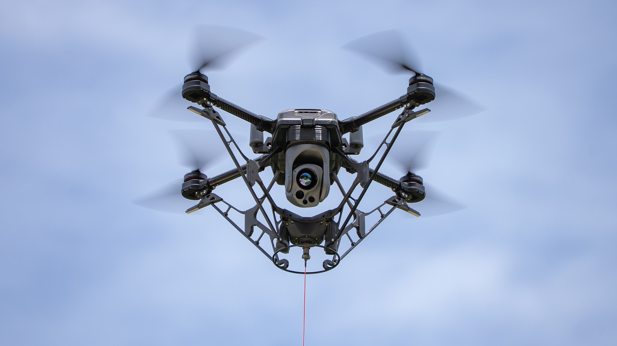 A small black drone is soaring through a clear blue sky, showcasing its sleek design and agile movement.