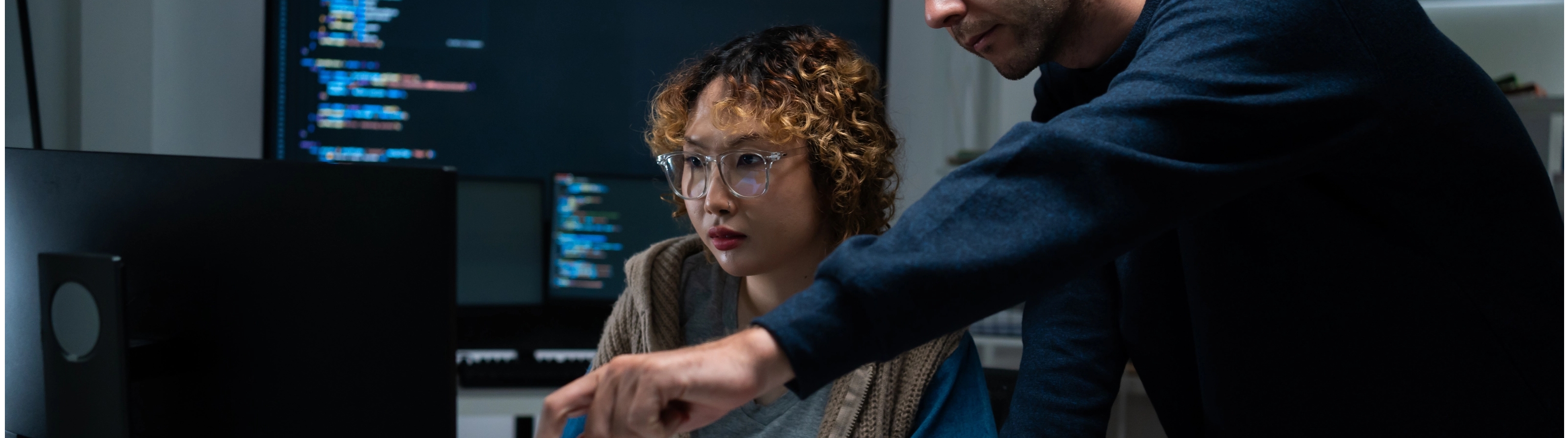 A man and woman collaborate on a computer, focused on their work in a modern office setting.