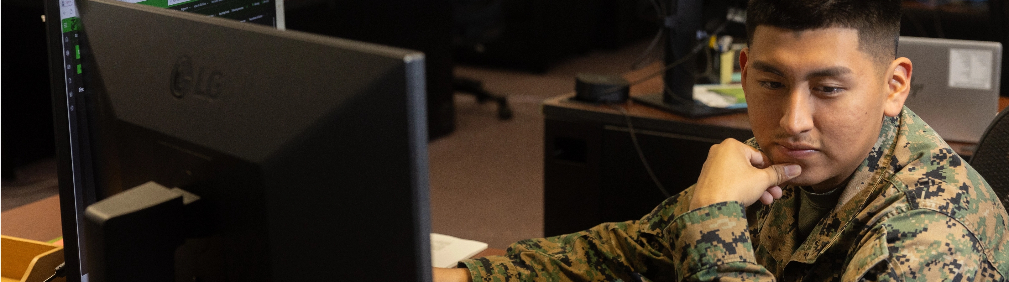A man in military uniform seated at a desk, focused on paperwork in a professional office setting.