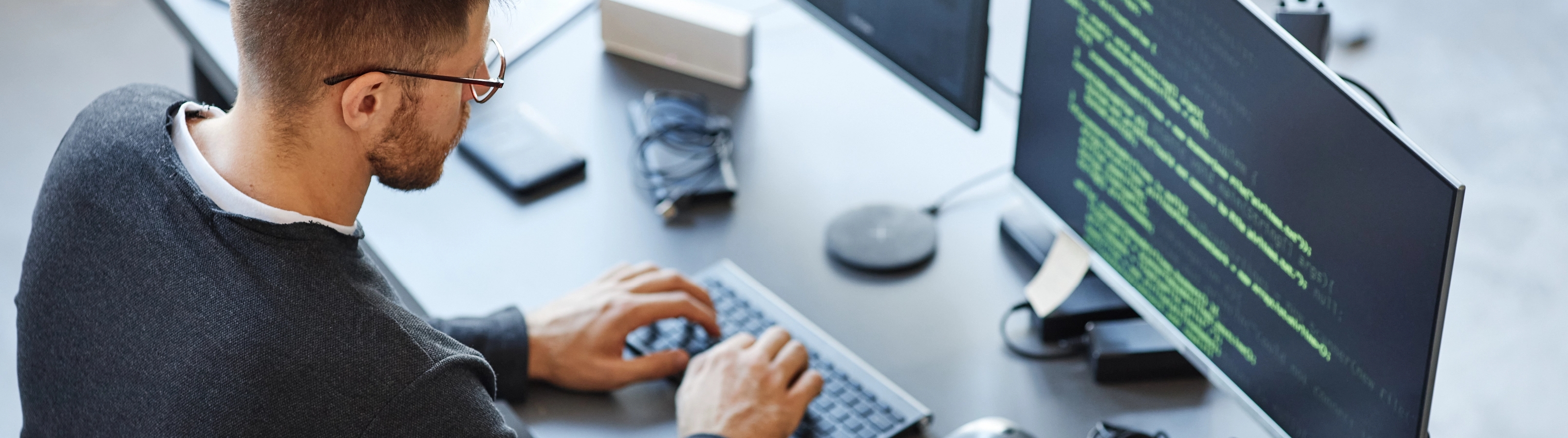 A man focused on typing on a computer keyboard, with a neutral background.