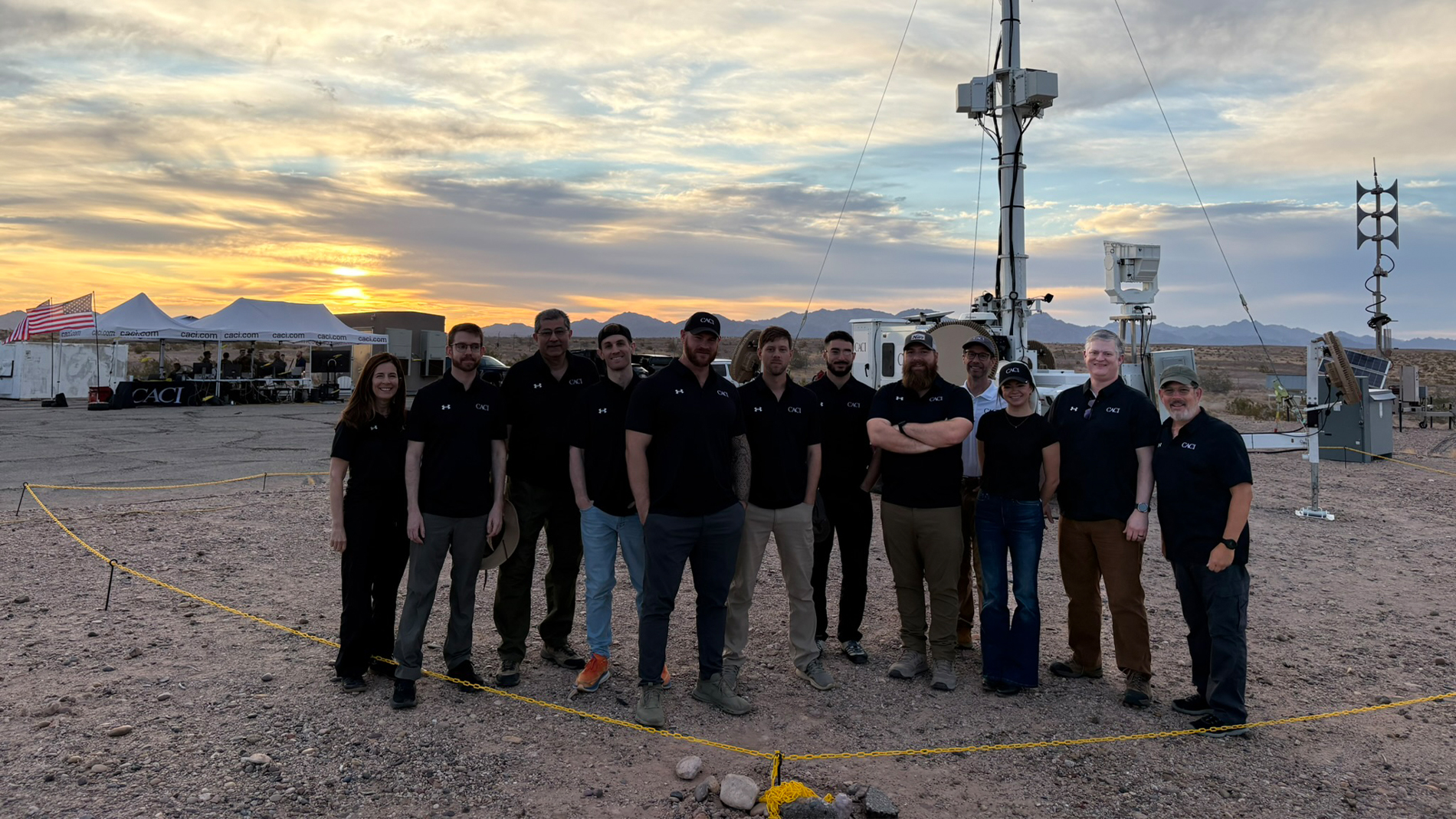 A group of five individuals stands together in front of a large communication antenna, smiling and posing for the photo.