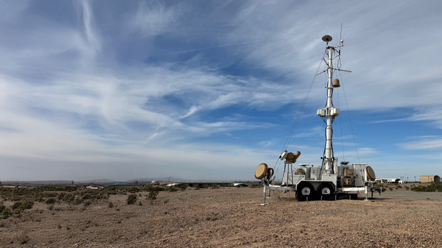 A tall metal tower with a satellite dish mounted at the top, set against a clear blue sky.