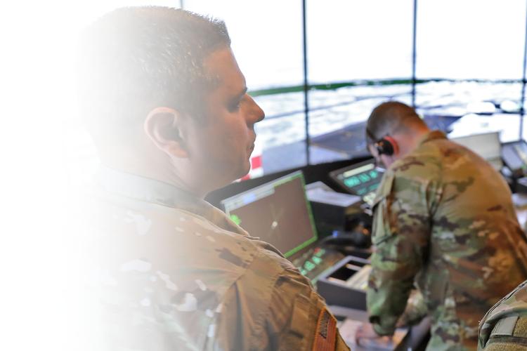 Two army soldiers examining a computer screen inside of a command and control center.