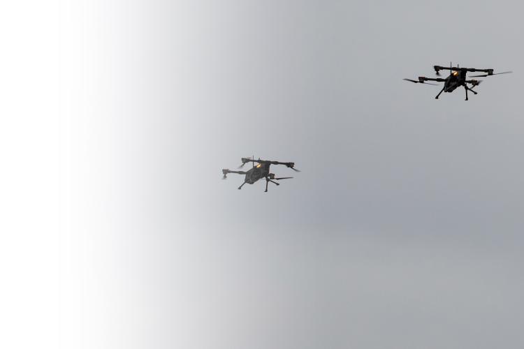 A formation of four drones flying closely together against a clear blue sky.