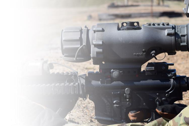 A soldier peers intently through the scope of a rifle, focused on a distant target.