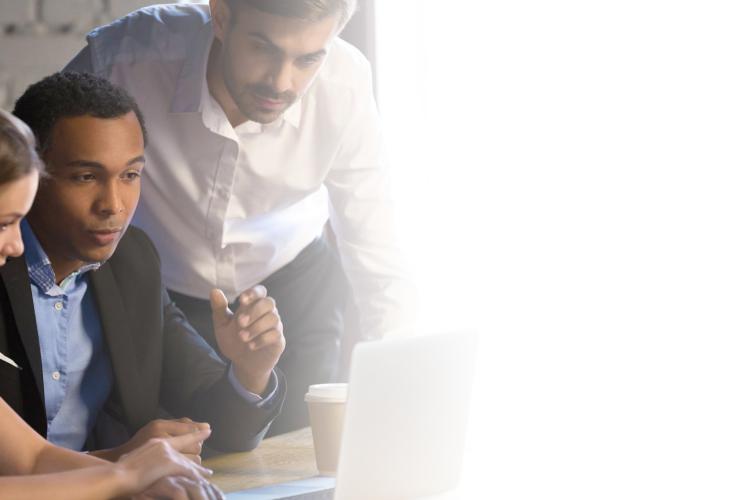 A diverse group of individuals gathered around a laptop, engaged in discussion and collaboration.