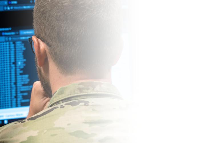 Two soldiers observe a computer screen intently, engaged in a discussion about the displayed information.