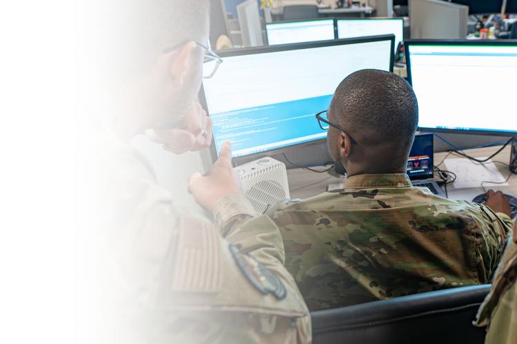 Three soldiers analyzing data on a computer screen.
