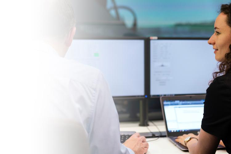 A woman and a man collaborate at a desk, engaged with their tasks while using several computer monitors.