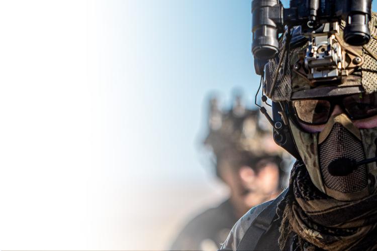 A soldier equipped with a helmet and goggles looking into the distance.