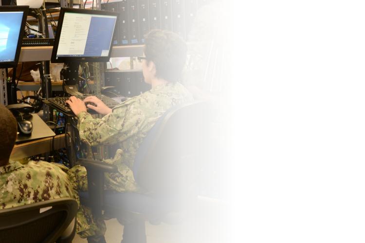 Two soldiers focused on their tasks while sitting at computers in a well-lit room, engaged in military operations.