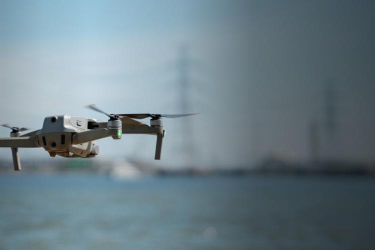 A small drone hovers above a tranquil body of water, capturing the serene landscape from above.
