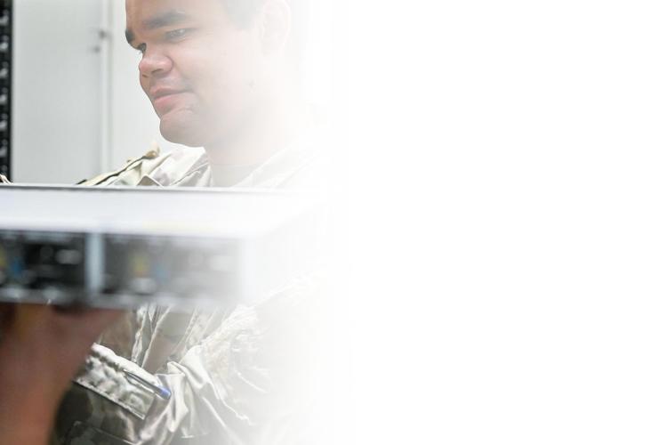 A soldier stands holding a server in front of a server rack, showcasing a blend of military and technology elements.
