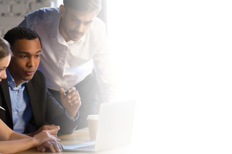 A group of people gathered around a laptop, engaged in discussion and looking at the screen together.