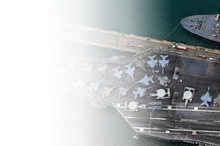 Aerial view of a large aircraft carrier surrounded by water, showcasing its deck and multiple aircraft positioned on it.