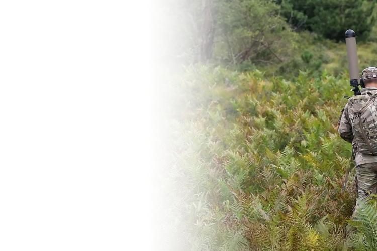 A man in camouflage walks through tall grass, blending into the natural surroundings.