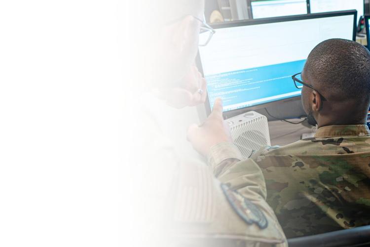 Two soldiers observe computer screens, focused on their tasks in a military setting.