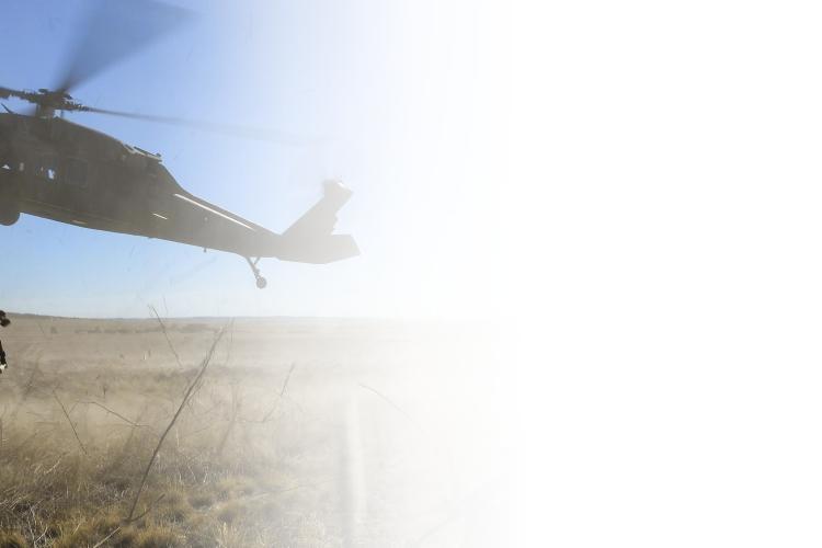 A soldier stands confidently in front of a military helicopter, ready for deployment in a tactical environment.