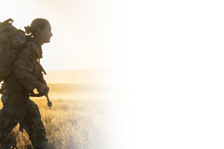  A woman in camouflage attire walking through a grassy field under a clear sky.
