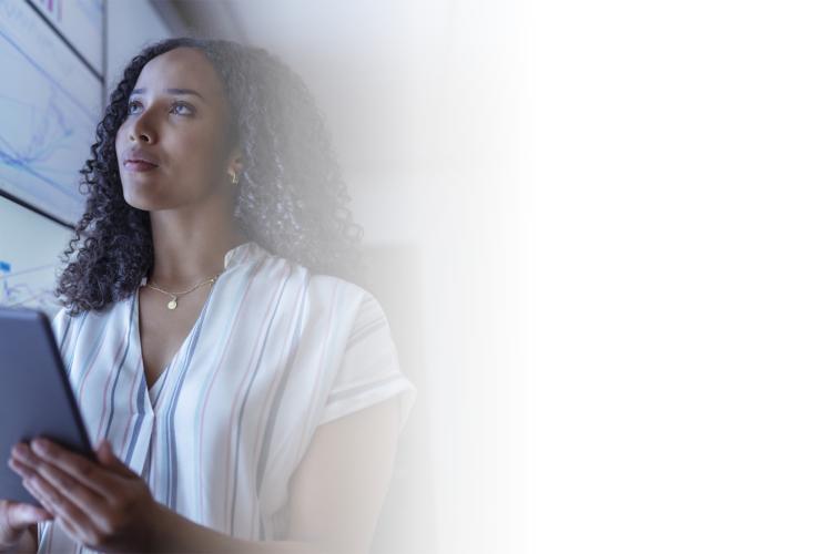 A woman holds a tablet in front of a large screen, engaged in a presentation or discussion.