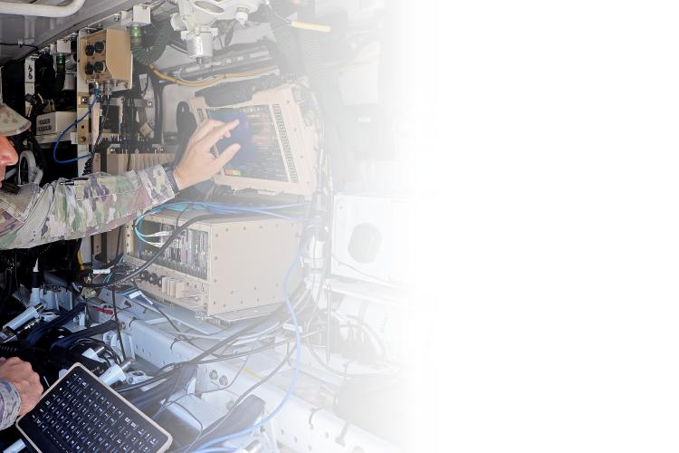 A soldier seated at a desk, focused on working on a laptop computer in a military setting.