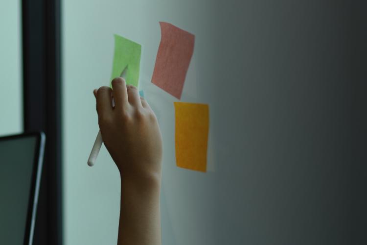  woman writing on a sticky note attached to a whiteboard, focused on organizing her thoughts.
