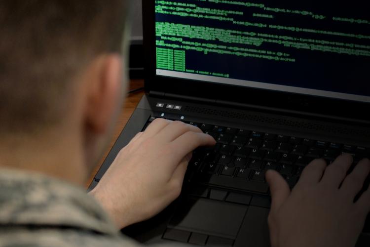 A soldier in uniform is focused on typing on a laptop computer in a military setting.
