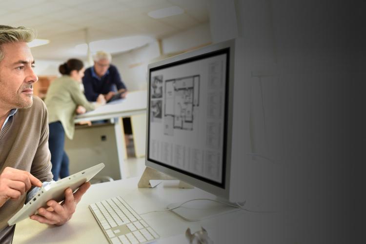 A man sits at a desk, focused on a tablet computer in front of him.