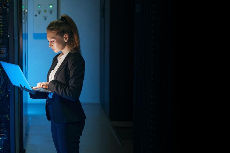 A woman in a suit stands confidently in front of a server, showcasing her professional presence in a tech environment.