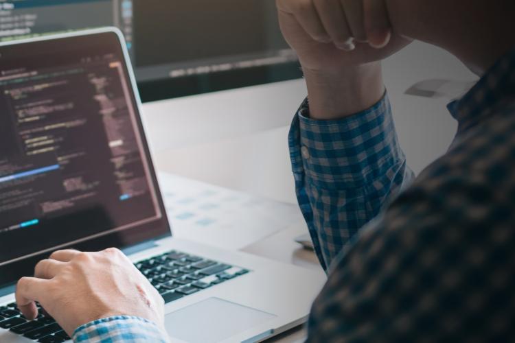 A person seated at a desk, working on a laptop with a computer screen in front of them.