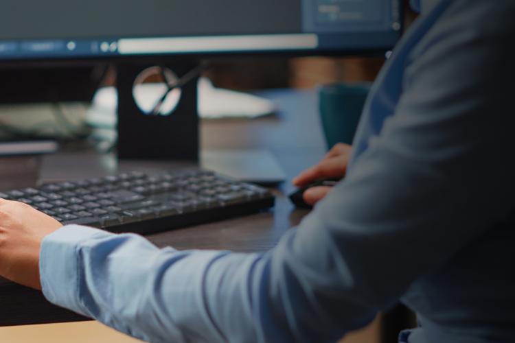 A person typing on a keyboard, focused on three computer monitors displaying various applications.