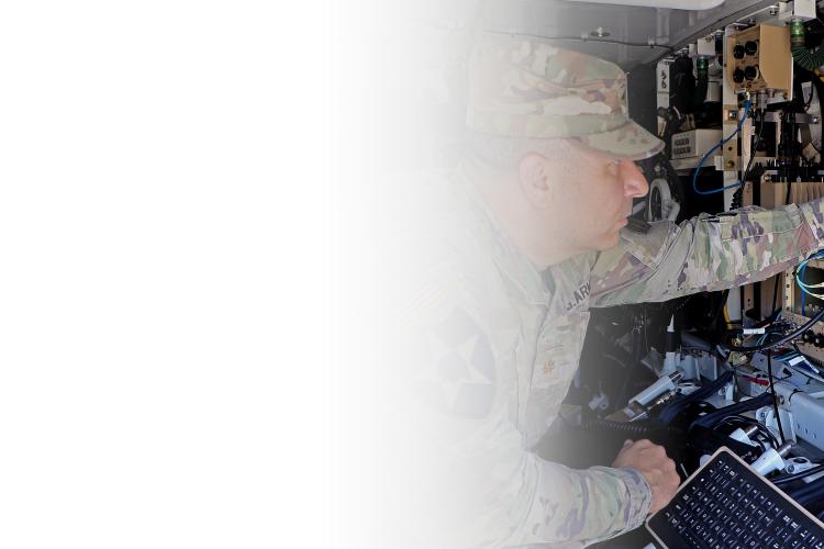 A soldier focused on a laptop computer, working diligently in a military setting.