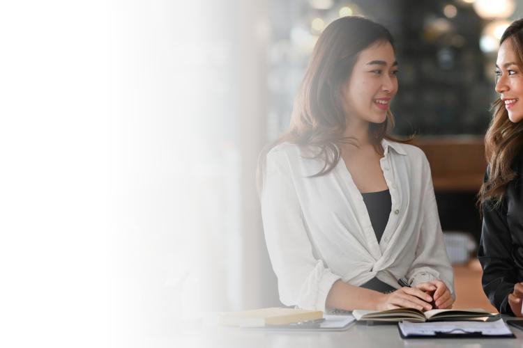Two women seated at a table, collaborating on a laptop, engaged in discussion and sharing ideas.