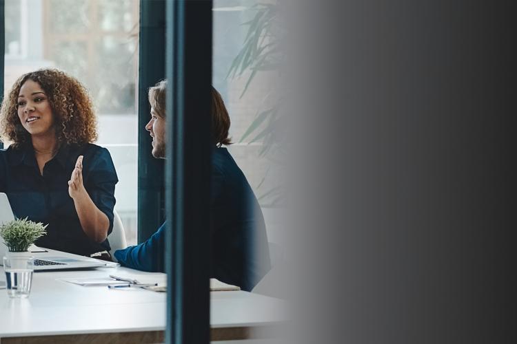 A group of diverse individuals seated around a table engaged in discussion in a meeting room.