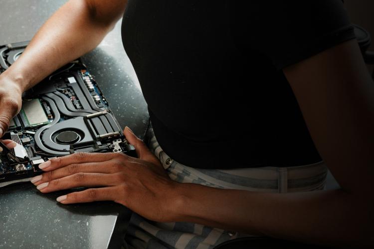 A person focused on a laptop, writing notes with a pen in a well-lit workspace.