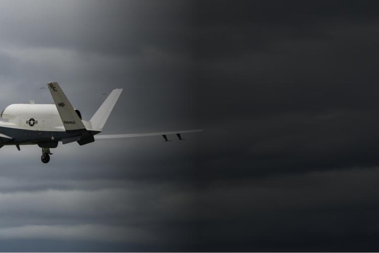 A military drone soaring through a cloudy sky, with dark clouds looming in the background.