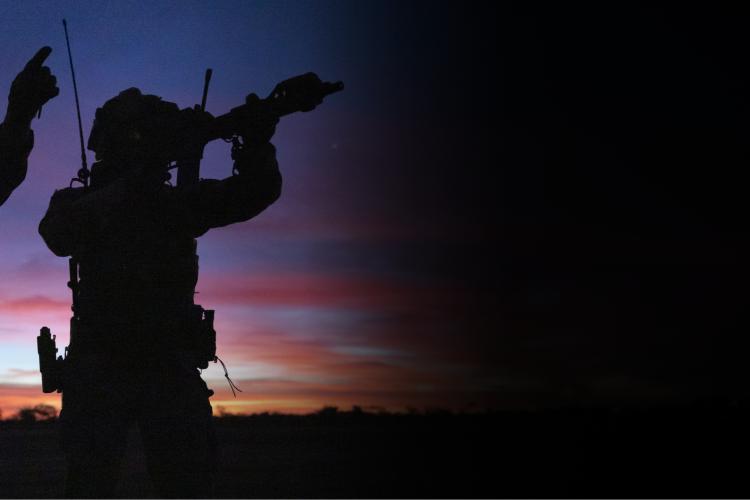 Two soldiers silhouetted against a vibrant sunset sky, creating a striking contrast of dark figures and colorful clouds.