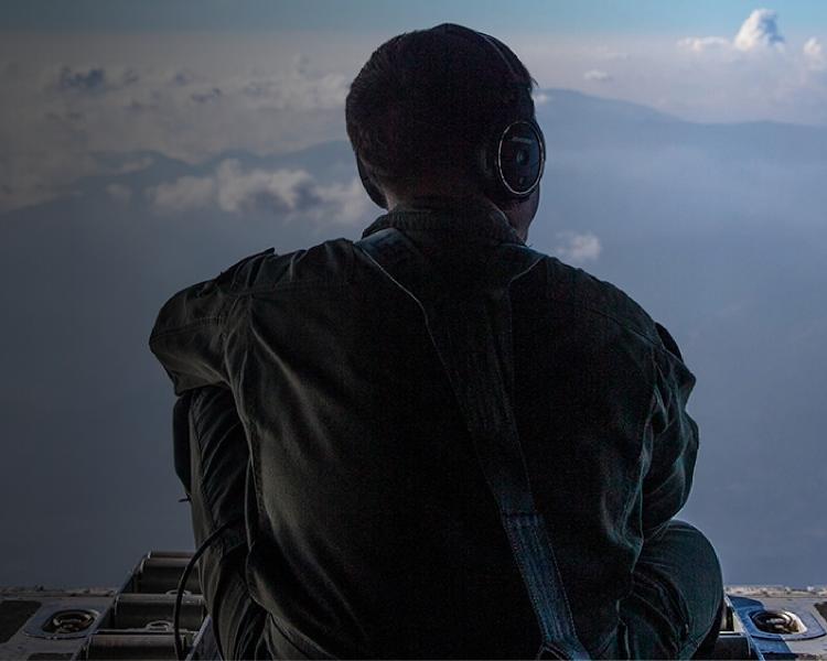A man in an aircraft, gazing out over the vast ocean under a clear blue sky.