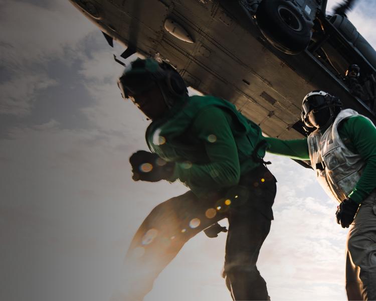 Two military personal outside a military helicopter.