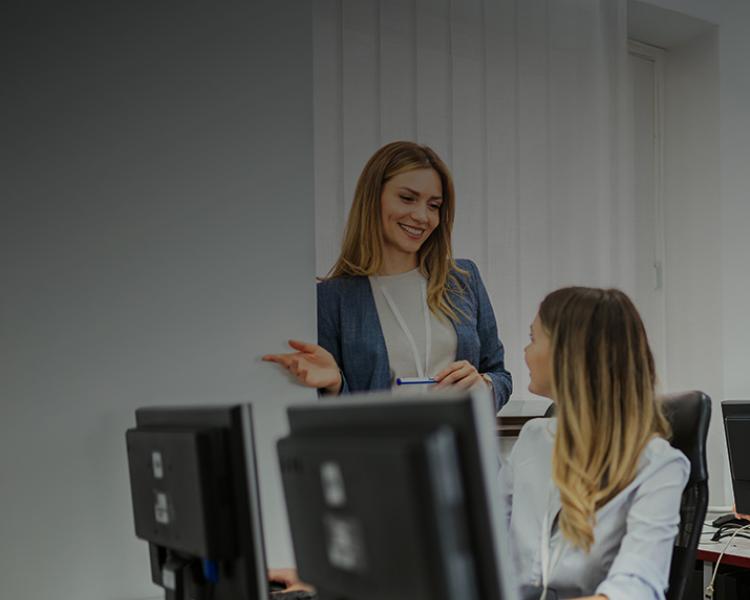 A man and woman sit at a desk, focused on a computer screen in a collaborative work environment.