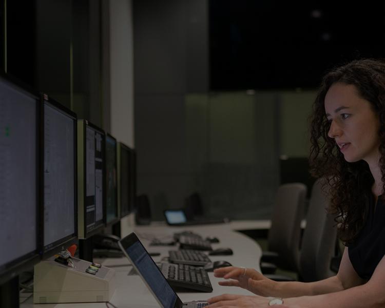 A woman in a black shirt gazes intently at a computer screen, focused on her work or research.