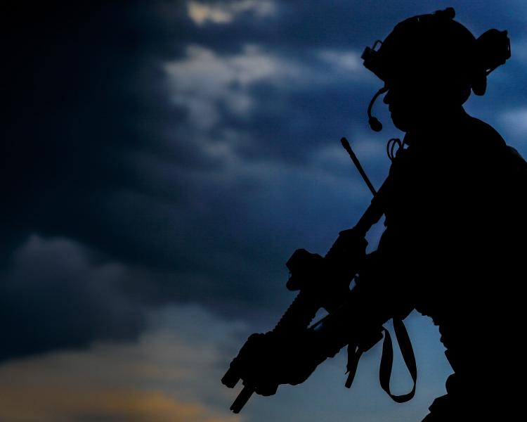 Silhouette of three soldiers standing resolutely against a dark, cloudy sky at dusk.